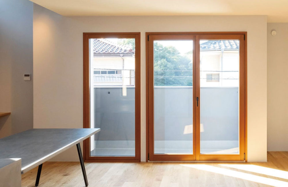 バルコニーに面して木製サッシの大きなドレーキップ窓を設けた住宅の室内。